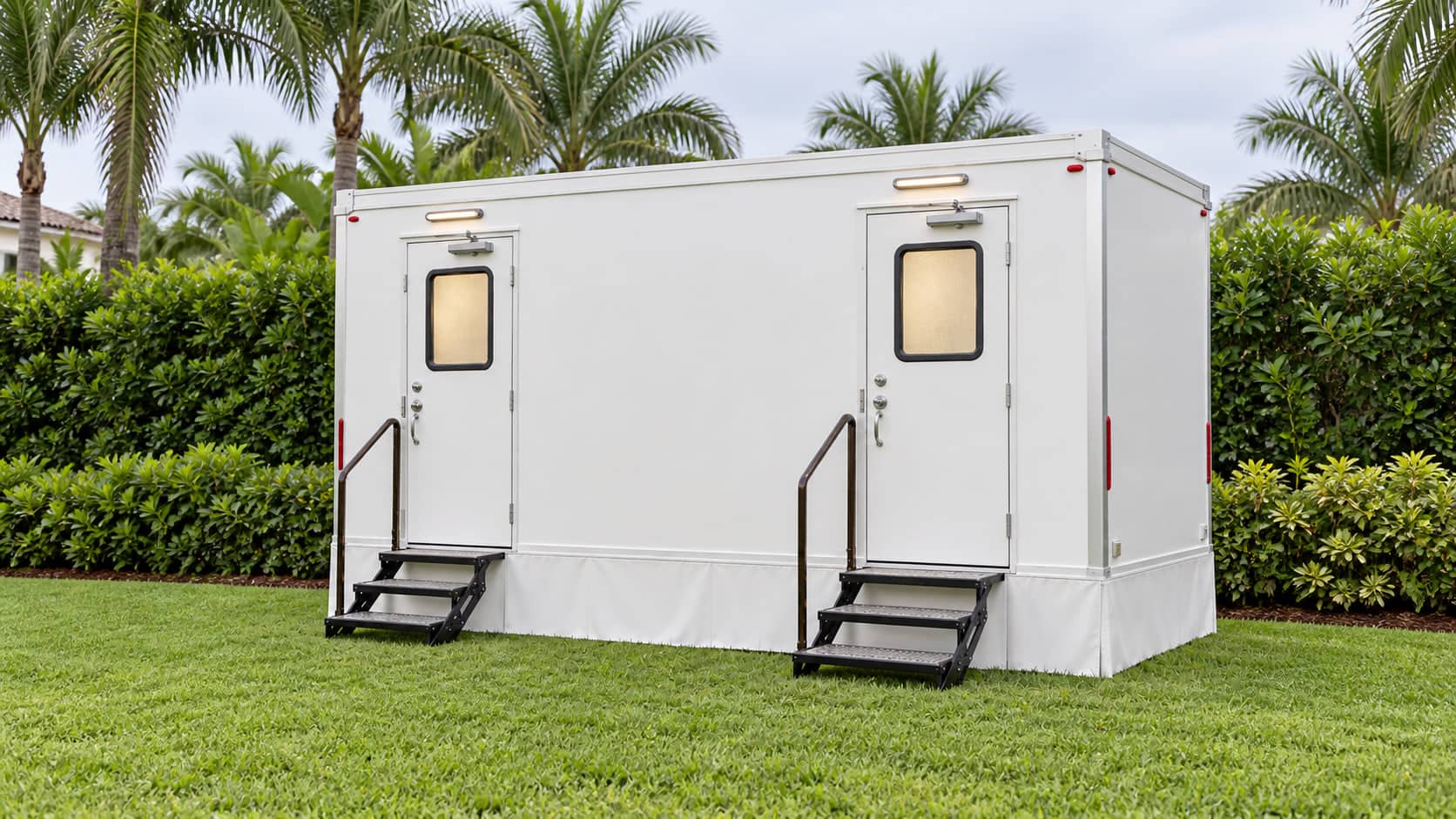 The full length of a two stall restroom trailer on grass, both doors closed, steps down at each